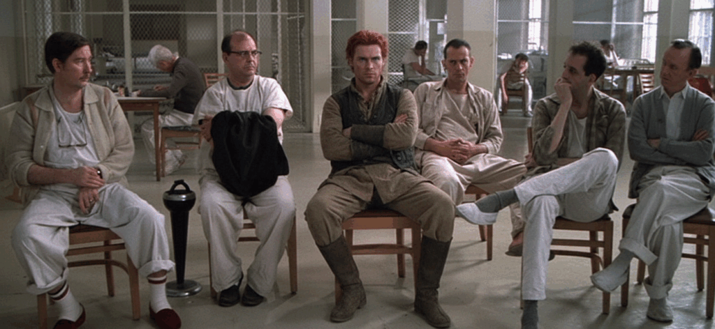 A screen capture from One Flew Over the Cuckoo's Nest. The original screen capture showed Jack Nicholson's character sitting in a chair flanked by other patients sitting in chairs. This modified image replaces Jack Nicholson with Rand al'Thor.