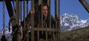A frame from the movie Willow (1988) showing Madmartigan trapped in a cage suspended above the ground.