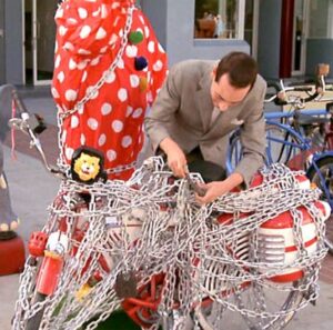 A frame from Pee-Wee Herman's Big Adventure where he is chaining his bike to a clown animatronic.